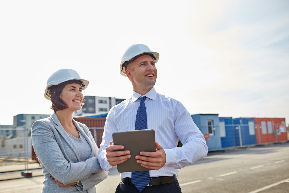 happy builders in hardhats with tablet pc outdoors
